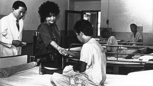 Accompanied by amfAR grantee Dr. Praphan Phanuphak, Elizabeth Taylor greets an AIDS patient in Bangkok, Thailand, in 1989.