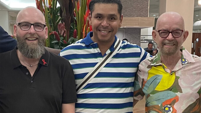 Three men smiling at an HIV awareness event with plants in the background.