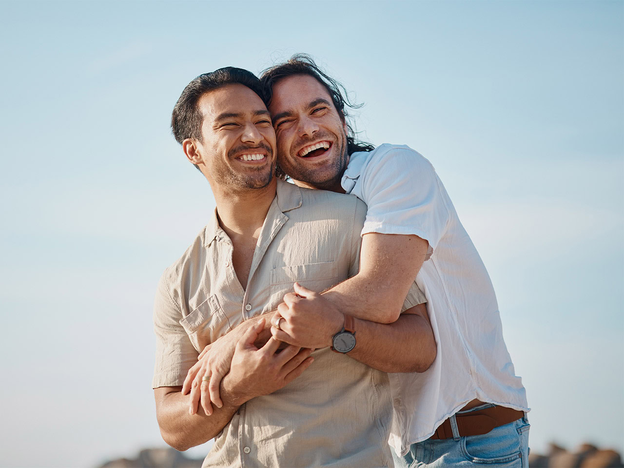 Two men smiling and hugging outdoors on a sunny day.