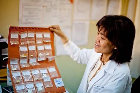 Female healthcare worker in a white coat reviewing labeled medication packets on an orange pill organizer chart.