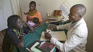 A healthcare worker consults with a woman seated beside a child in a small clinic.
