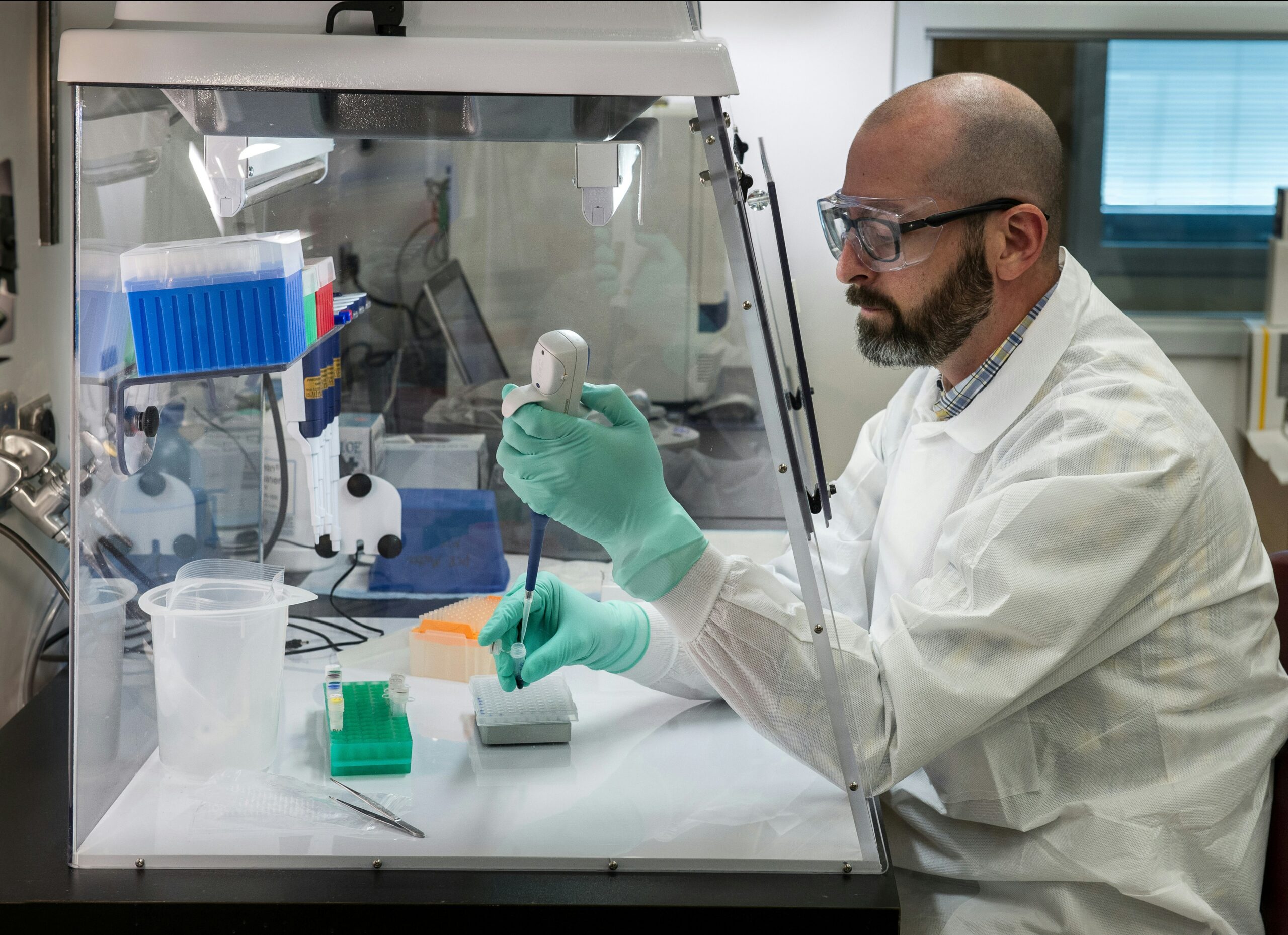 Researcher in a lab coat and gloves using a pipette at a laboratory workstation