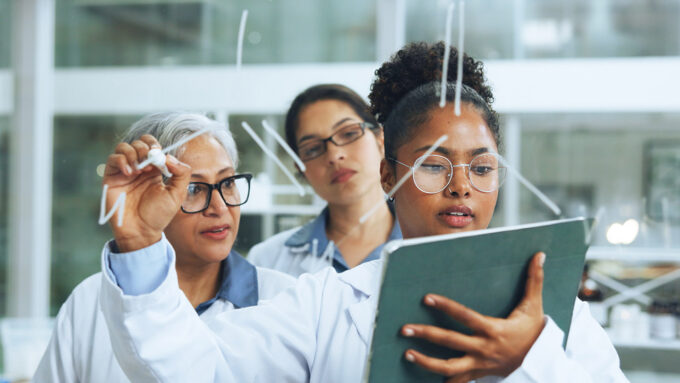 Group of diverse women scientists in lab examining data on a tablet.