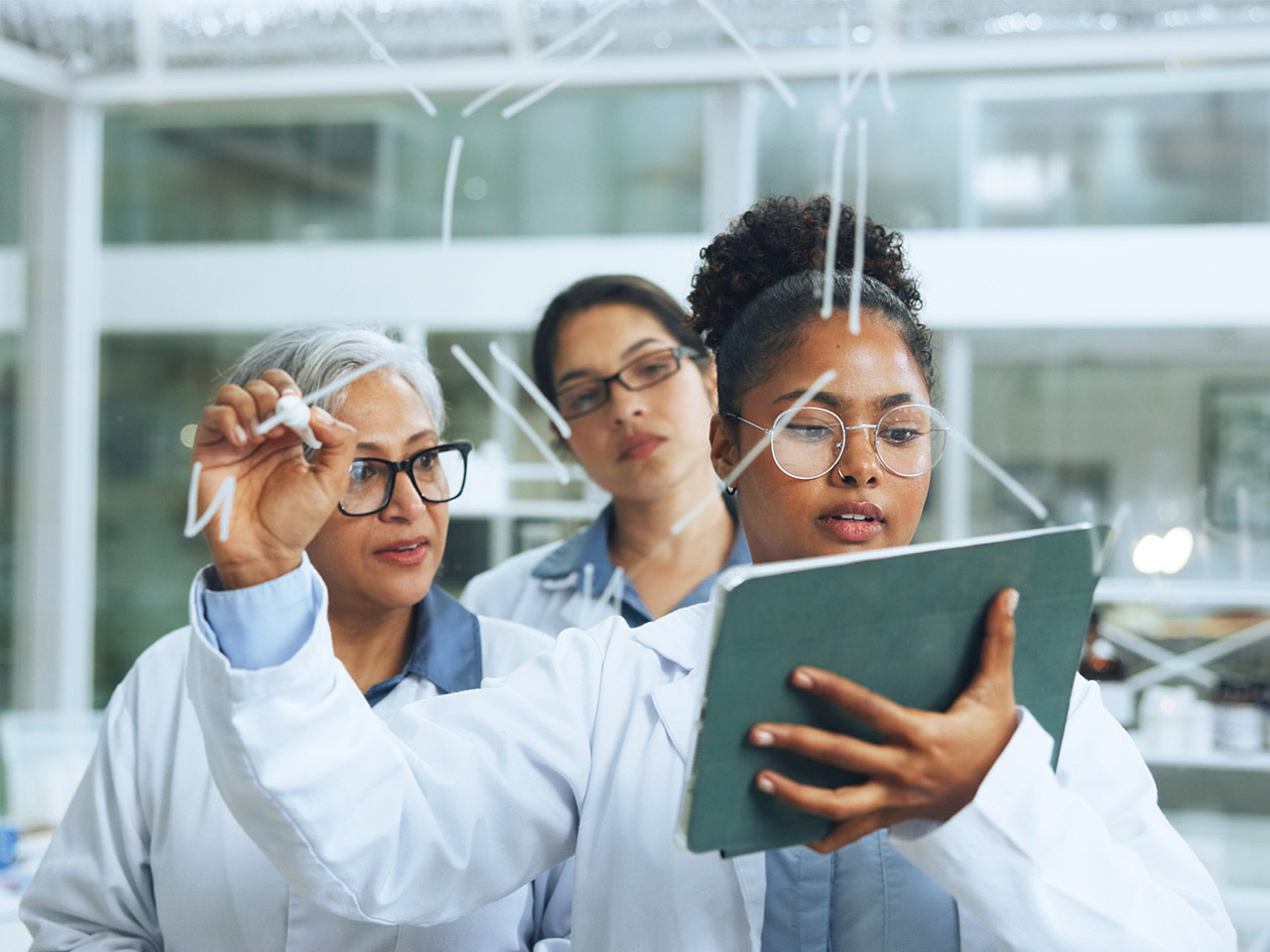 Group of diverse women scientists in lab examining data on a tablet.