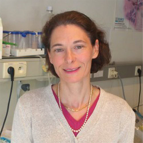Portrait of a female researcher in a clinical setting, smiling at the camera.